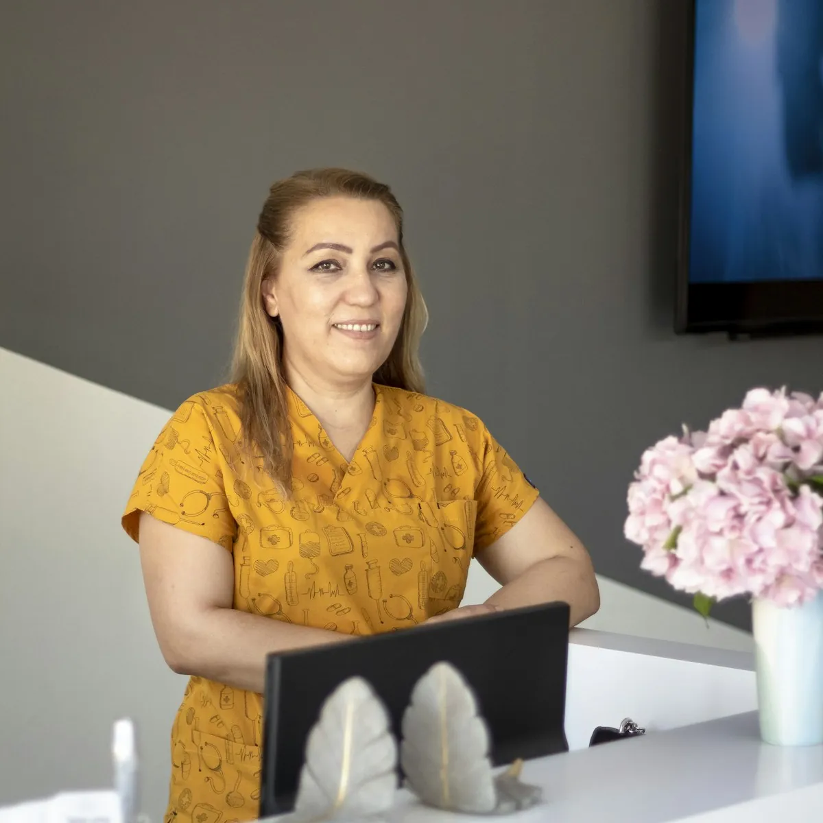 Smiling medical practice receptionist in scrubs standing at a clinic front desk